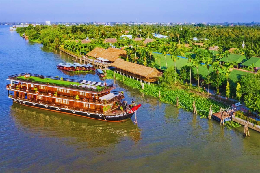 Funan Mekong River Cruise boat sailing along lush green riverbank with Auasia Travel